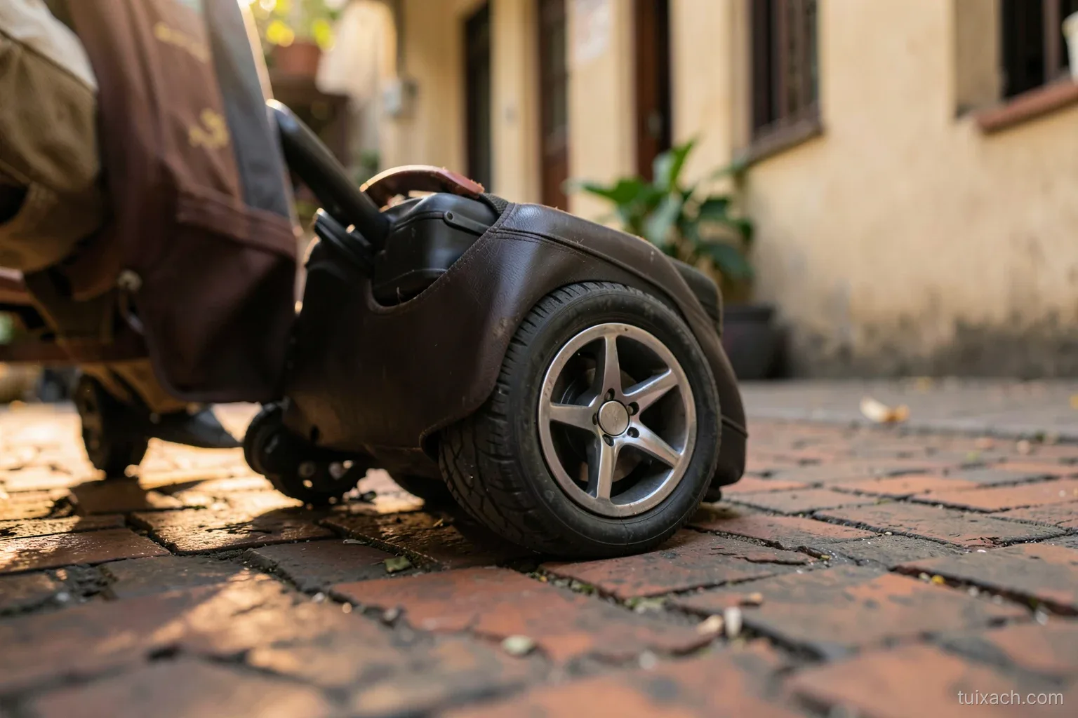 Low angle close-up of a suitcase double spinner wheel rolling over uneven brick pavement on a Vietnamese sidewalk, motion blur on the ground, late afternoon warm light